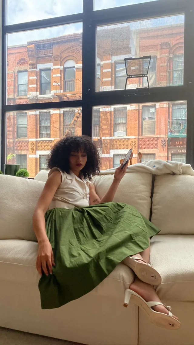 Whitney Peak sitting on a sofa in a pale top, green skirt and light shoes.
