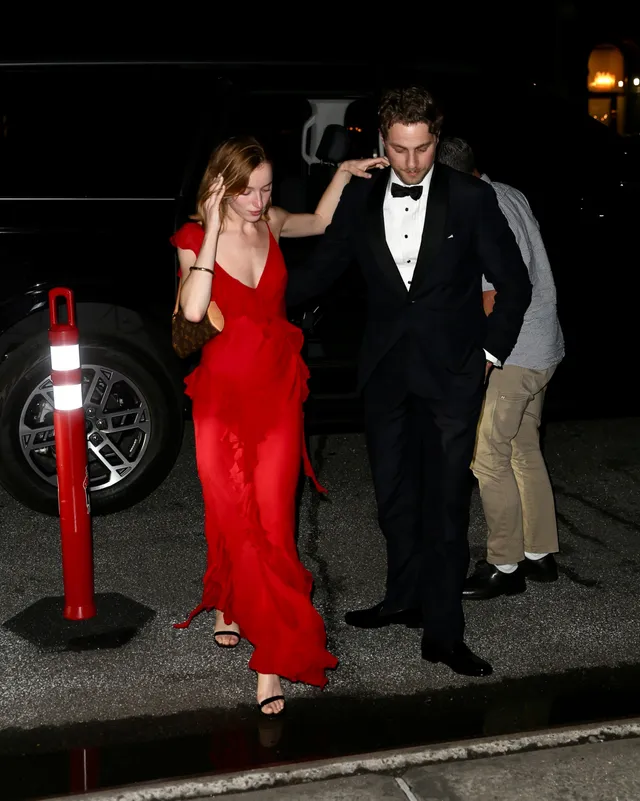 Phoebe Dynevor arriving in a red dress beside a companion.