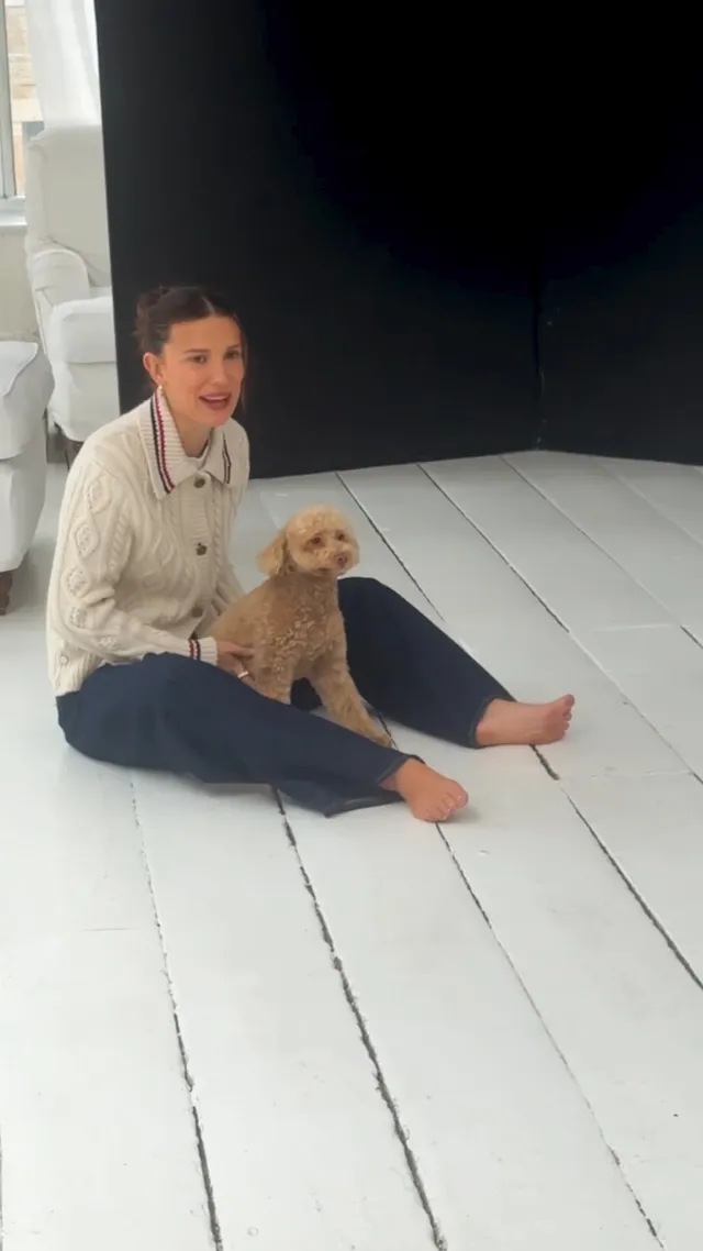 Millie Bobby Brown sitting beside a dog on a wooden floor.