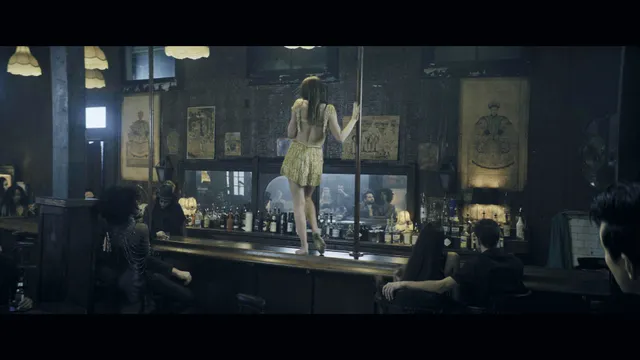Rebecca Ferguson standing barefoot on a bar counter in a yellow dress in a film scene.