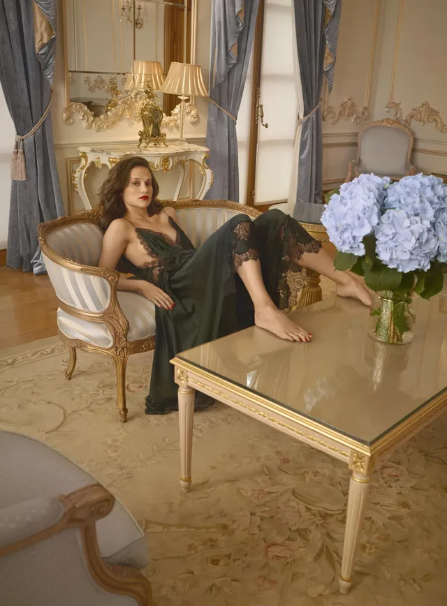 Alicia Vikander reclining on a sofa in an ornate room.