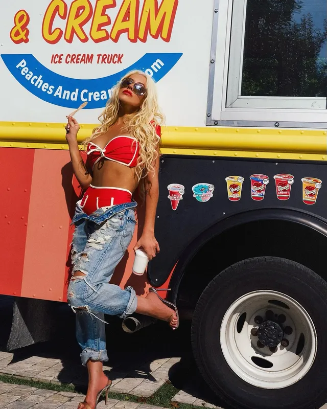 Christina Aguilera posing beside an ice-cream van with a heeled shoe raised.