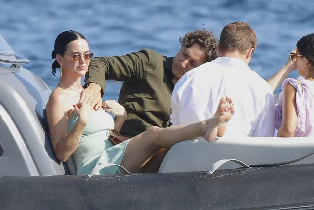 Katy Perry sitting aboard a boat with bare soles visible.