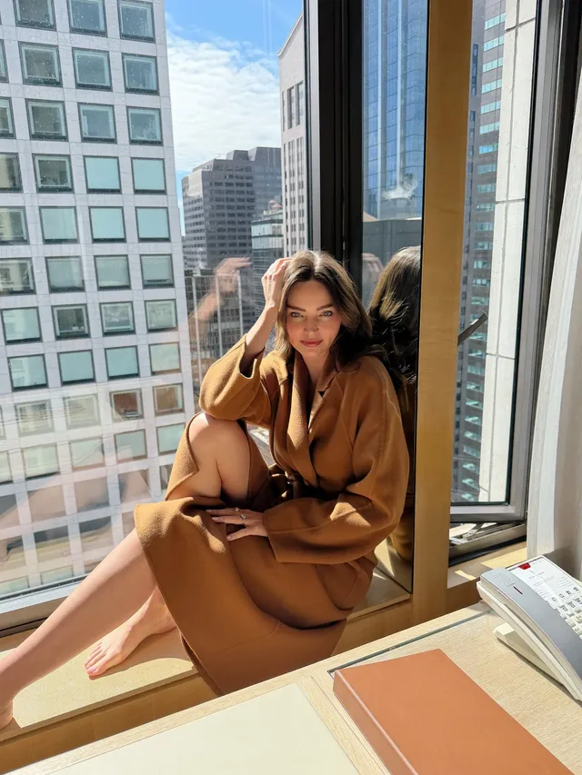 Miranda Kerr a barefoot seated portrait beside a city window.