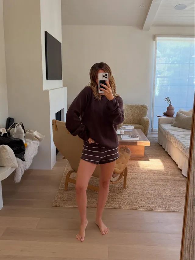 Ashley Tisdale taking a barefoot mirror photograph in a dark sweatshirt and shorts.