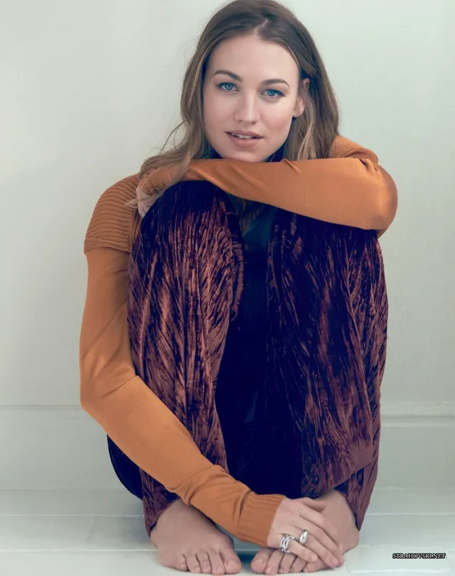 Yvonne Strahovski sitting in a chair in a patterned skirt.