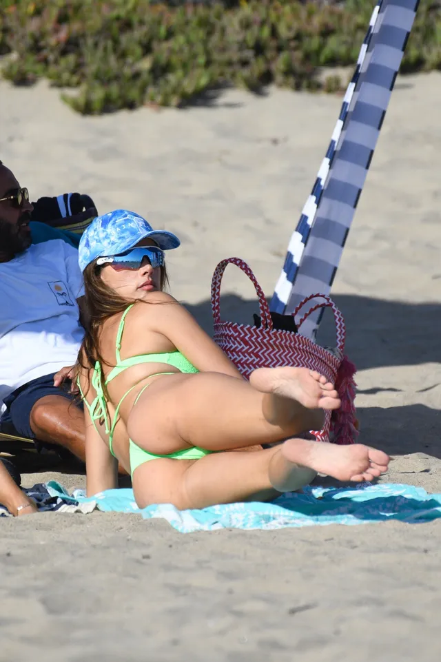 Alessandra Ambrosio reclining on a beach with bare soles visible.