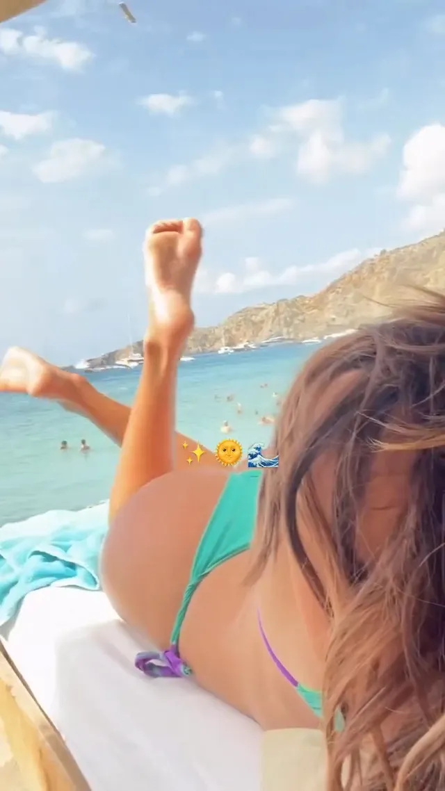 María Pedraza reclining barefoot on a lounger by the sea.