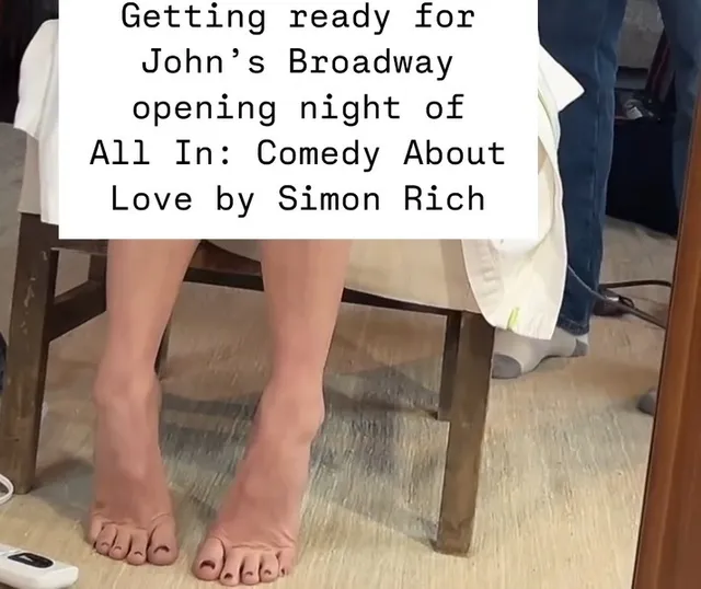Olivia Munn showing bare feet with dark-painted toenails beneath a pale outfit.