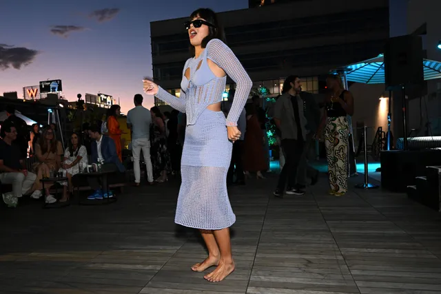 Xochitl Gomez standing barefoot outdoors at dusk in a lavender dress.