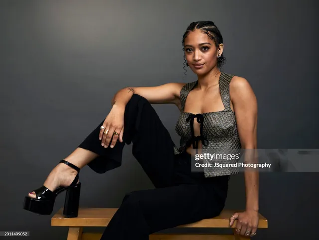 Samantha Logan posing on a wooden bench in a dark outfit and platform heels.