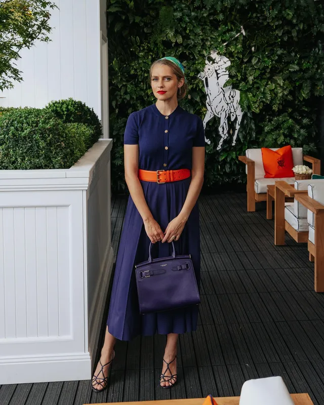 Teresa Palmer standing on a patio in a navy dress.