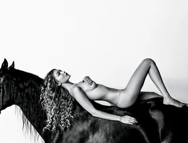 Gigi Hadid reclining barefoot beside a horse for a monochrome portrait.