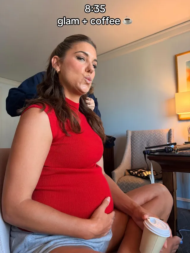 Alex Morgan sitting barefoot in a chair in a red top during a maternity portrait.