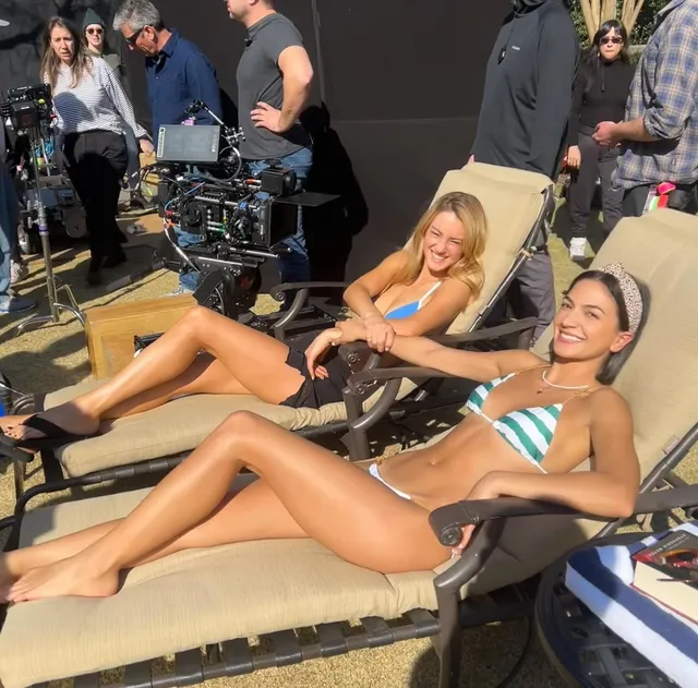 Grace Van Patten relaxing barefoot beside another woman on a film set.
