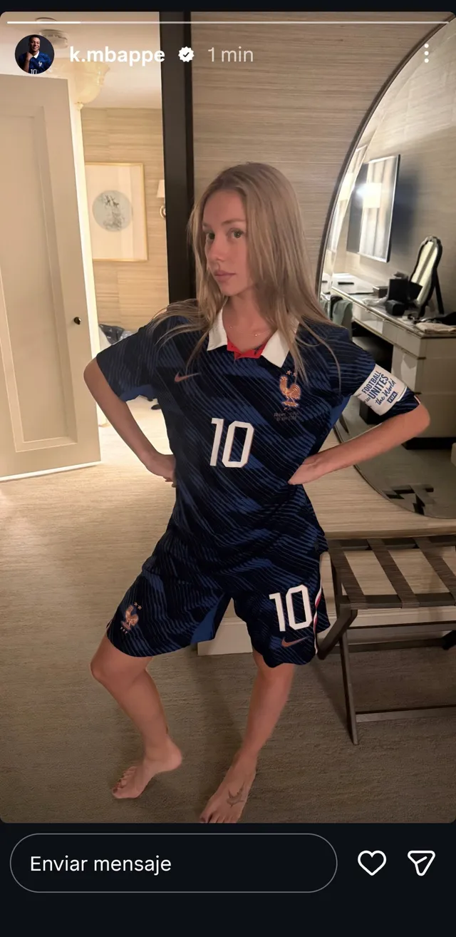 Ester Expósito standing barefoot in a football jersey and shorts indoors.
