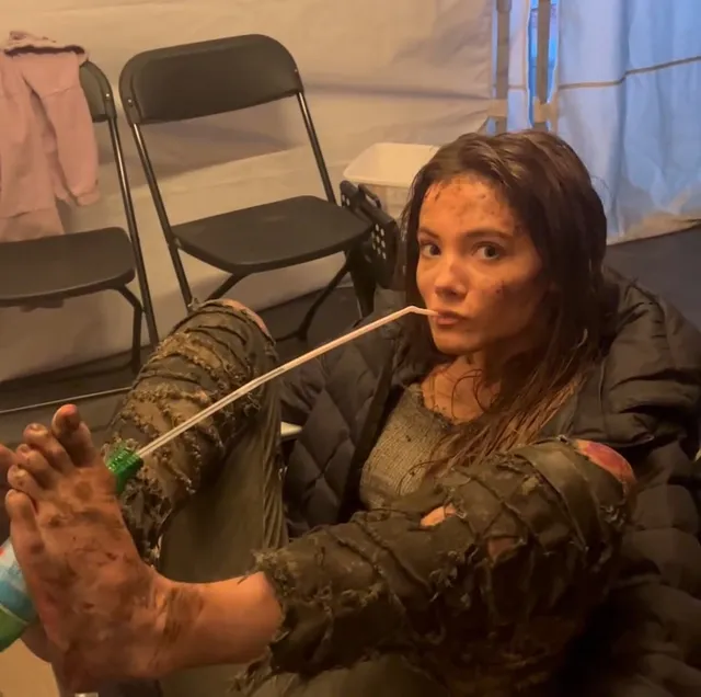 Freya Allan resting with her bare soles facing the camera on a film set.