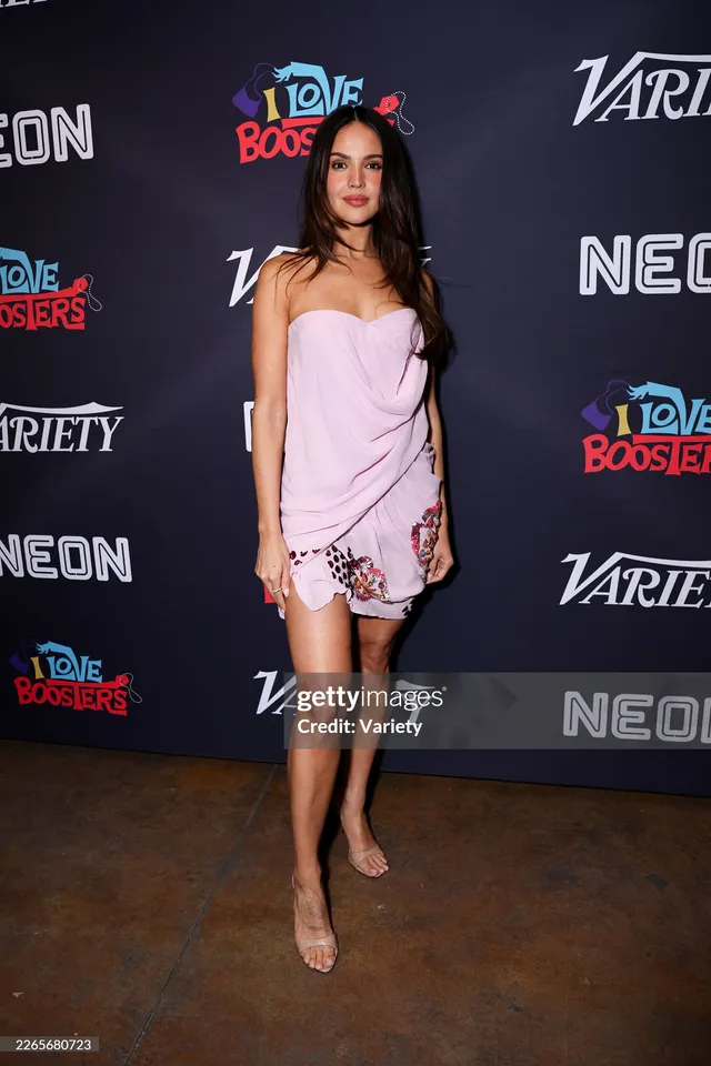 Eiza González posing in a pale patterned outfit and heels at an event.