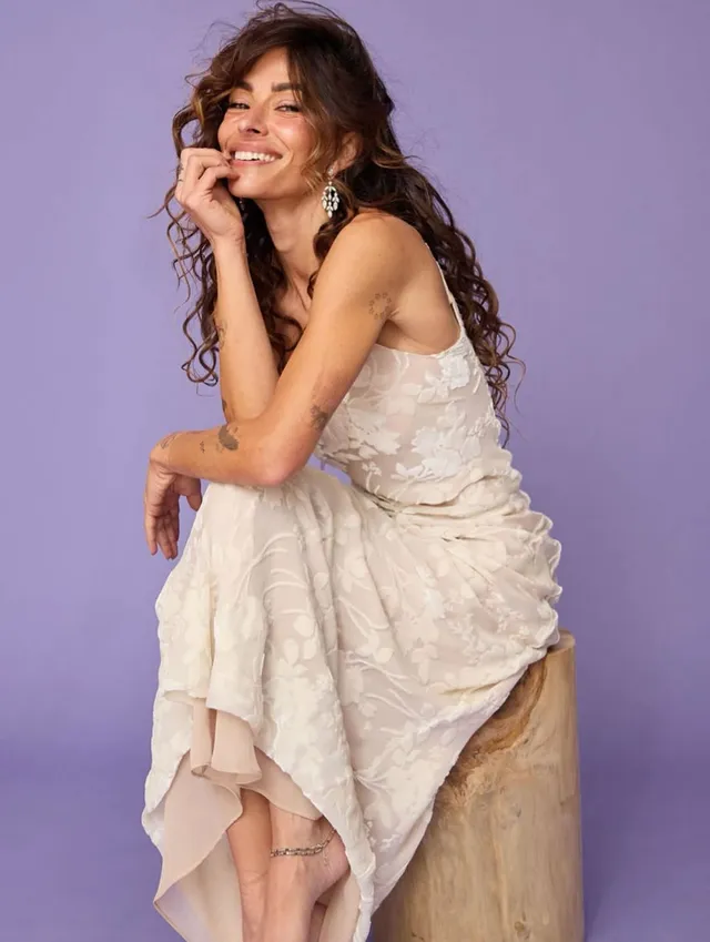 Sarah Shahi sitting for a portrait in a pale dress.