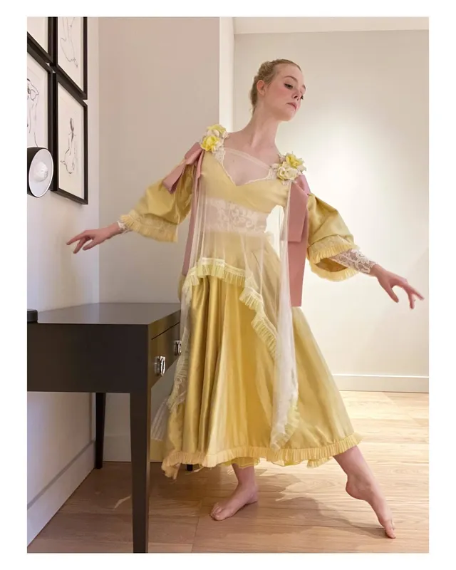Elle Fanning posing barefoot indoors in a yellow dress.