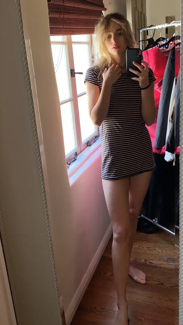 Suki Waterhouse taking a mirror photograph in a short striped dress.