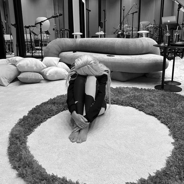 Christina Aguilera sitting barefoot on a rug in a monochrome portrait.