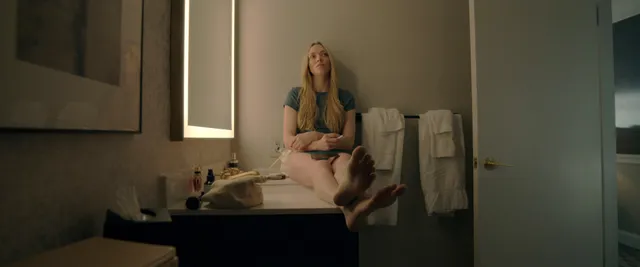 Amanda Seyfried sitting barefoot on a bathroom counter beside towels.