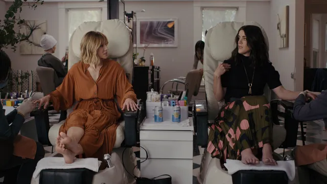 Kristen Bell sitting barefoot at a pedicure station beside another person.