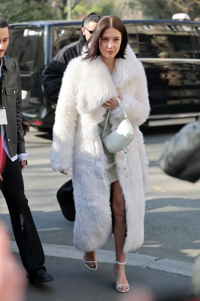 Adèle Exarchopoulos walking outside in a white coat and sandals.