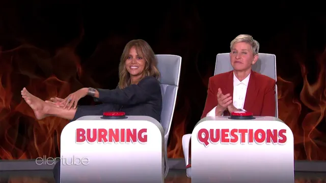 Halle Berry sitting barefoot on a television set beside the host.