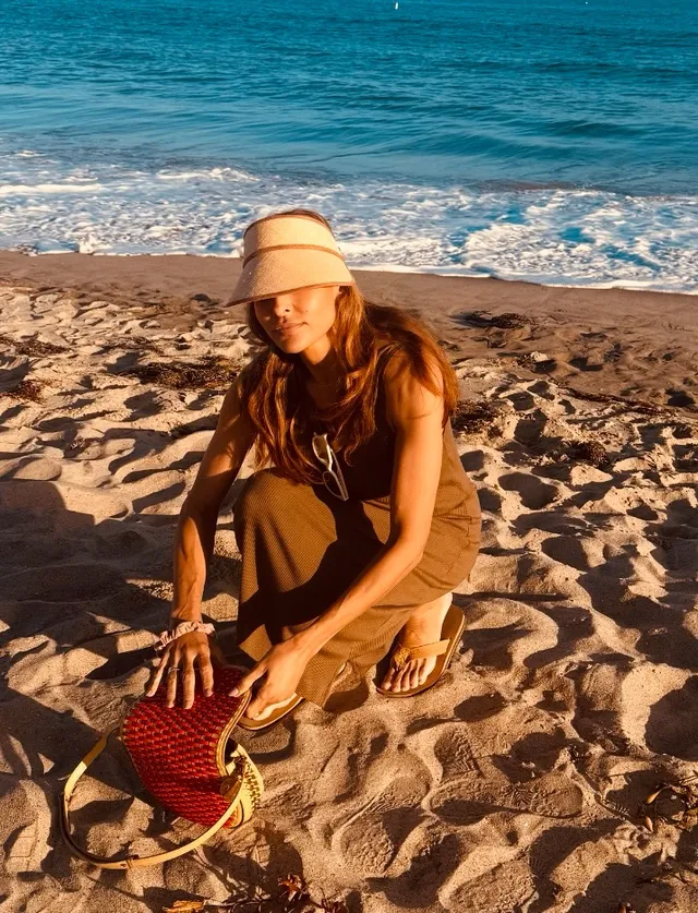 Eva Mendes crouching on a beach in flat sandals.