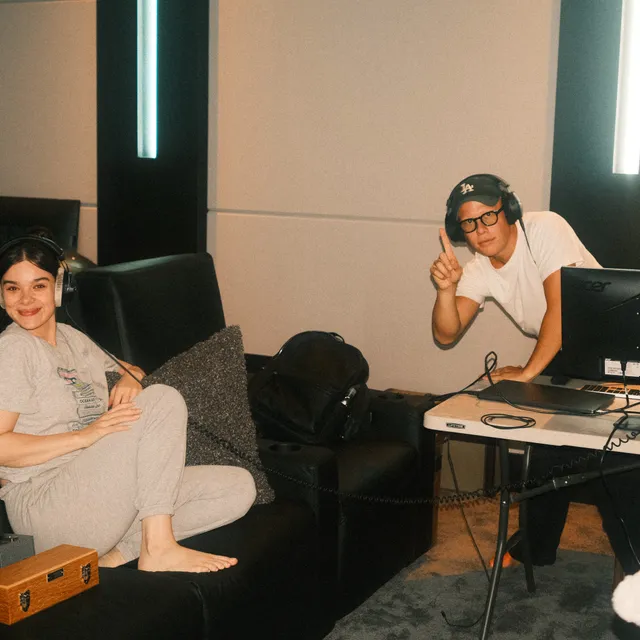Hailee Steinfeld sitting barefoot on a sofa during a recording session.