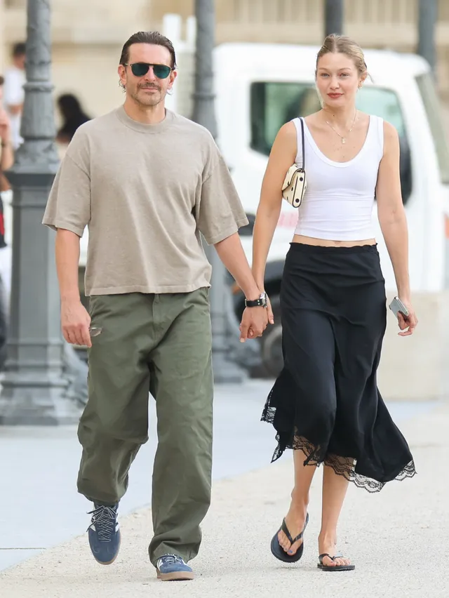 Gigi Hadid walking beside a companion in flat sandals.