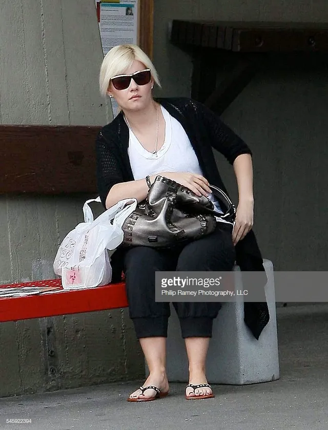 Elisha Cuthbert sitting outdoors in cropped trousers and flip-flops.
