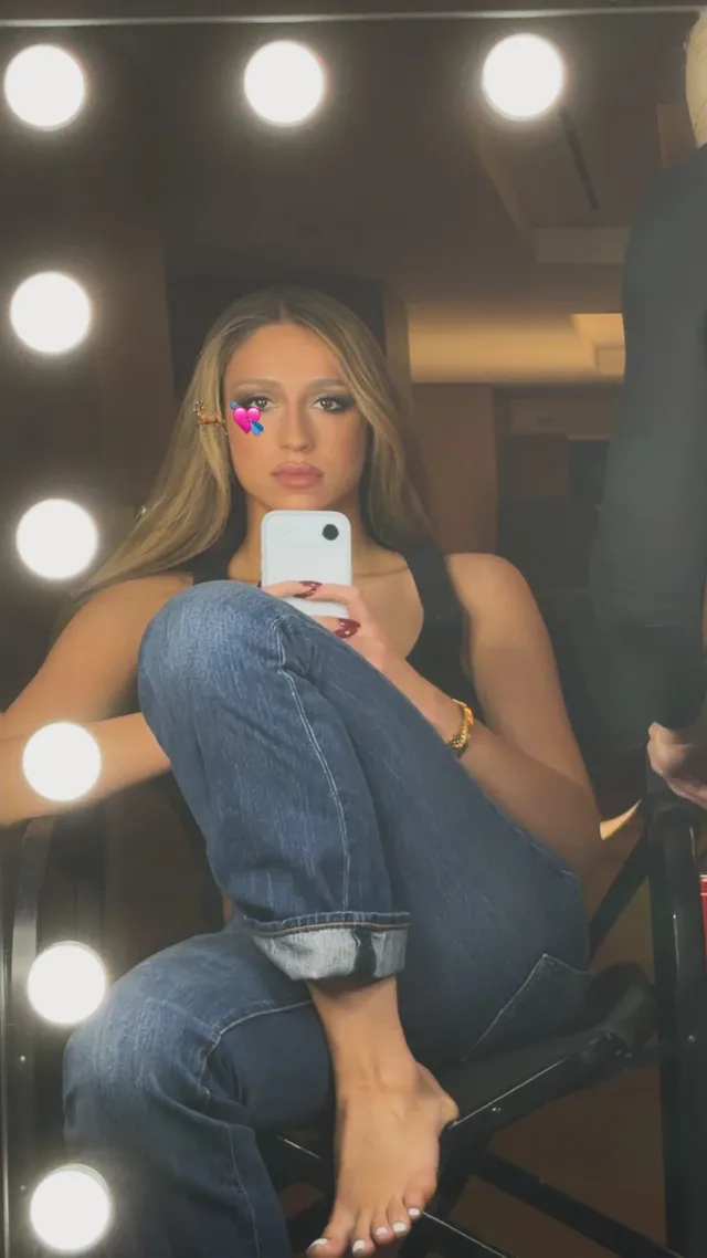 Tate McRae taking a mirror photo with bare feet visible.