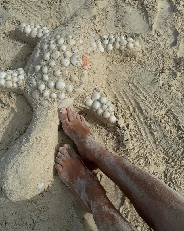 Irina Shayk bare feet on sand beside small shells.