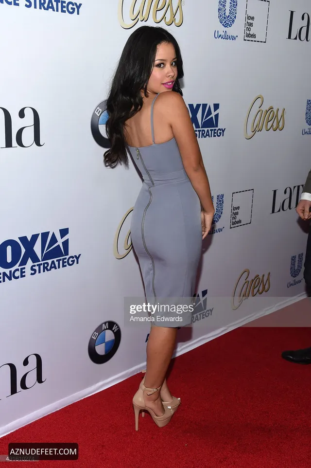 Cierra Ramirez in a gray fitted dress and pale heels looking over her shoulder.