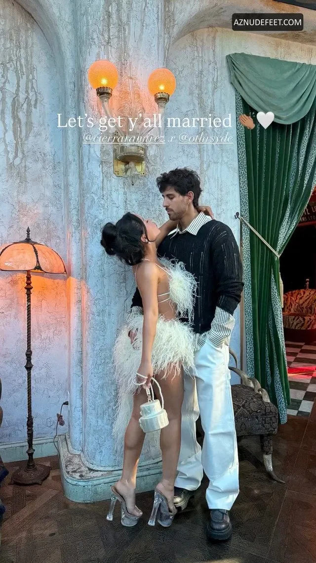 Cierra Ramirez in a white feathered dress and silver sandals embracing her partner.