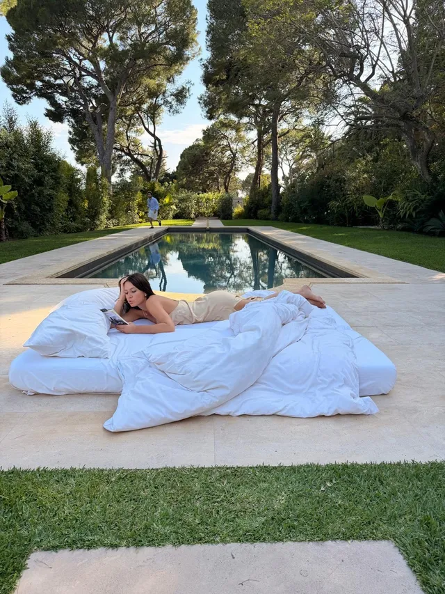 Adèle Exarchopoulos reclining beside a pool on white bedding.