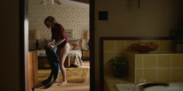 Elizabeth Olsen standing barefoot beside a doorway in a film scene.
