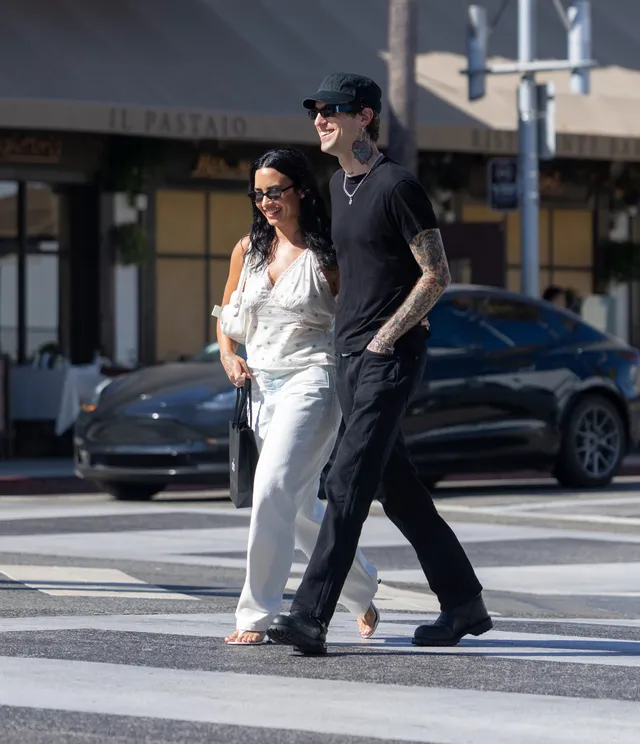 Demi Lovato walking outdoors in white trousers and flat sandals.