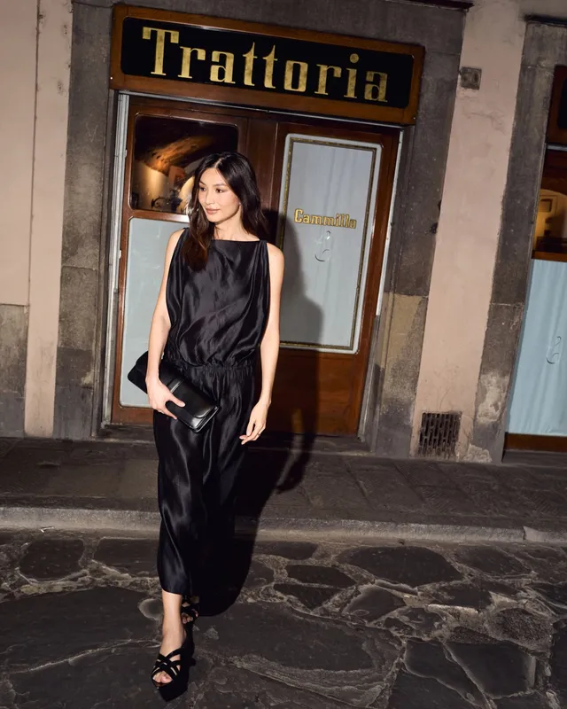 Gemma Chan standing outside a restaurant in a black outfit.