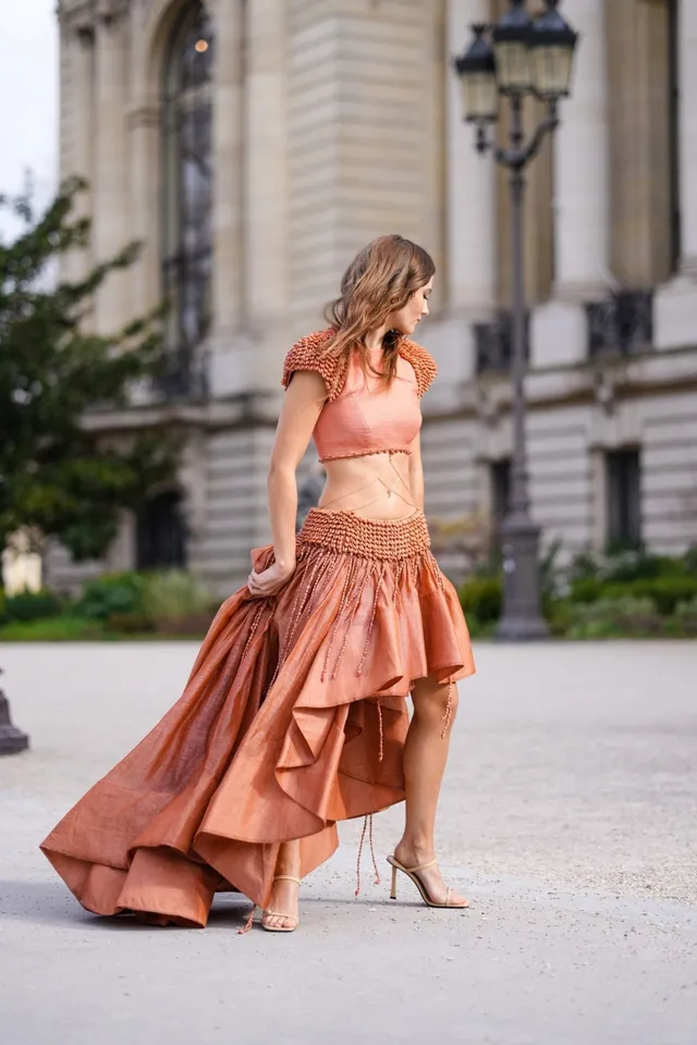 Freya Allan walking outdoors in an orange dress and pale heels.
