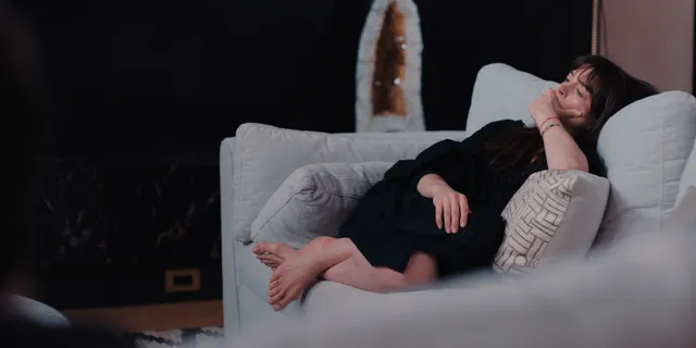 Anne Hathaway reclining barefoot on a pale sofa.