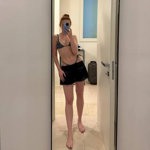 Madelaine Petsch standing barefoot in dark swimwear for a mirror photo.