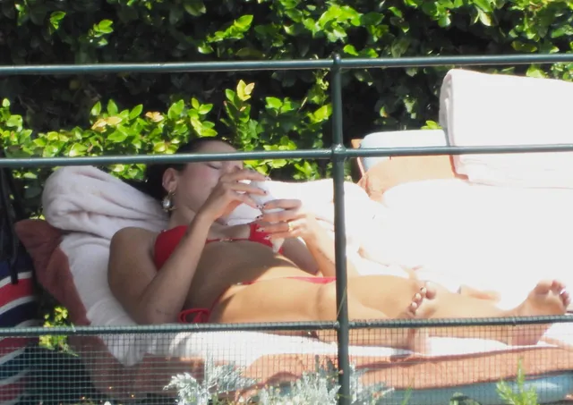 Dua Lipa lying barefoot on a striped lounger outdoors.