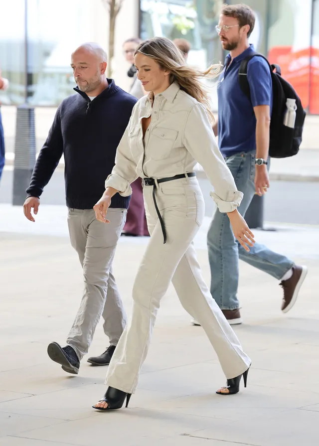 Jodie Comer walking past a venue in a pale outfit.