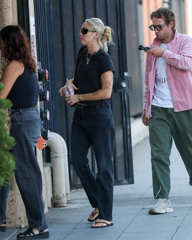 Miley Cyrus standing outside in jeans and flip-flops.