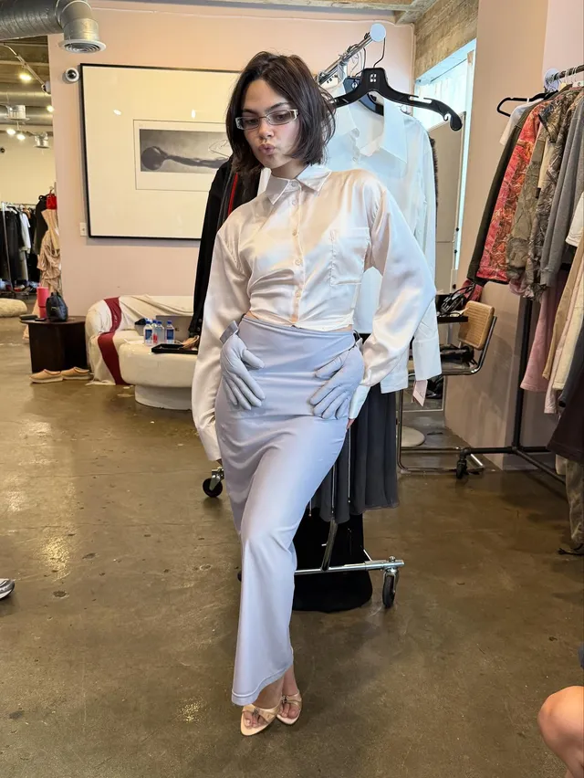Ariana Greenblatt standing indoors in a pale outfit and metallic heels.