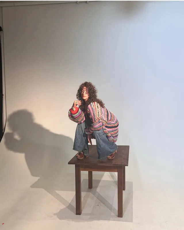 Odessa A'zion posing on a wooden table in brown heels.